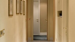 Um corredor com uma porta no final, quadros nas paredes e um interruptor de luz à esquerda.