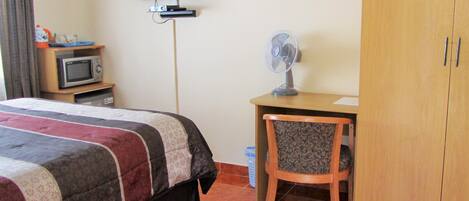 Una habitación de hotel con una cama, un escritorio con silla, televisión, microondas y ventilador.
