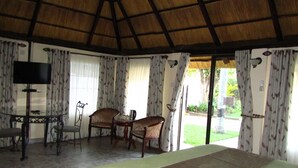 A room with a bed, a TV, two chairs, a table, and curtains.