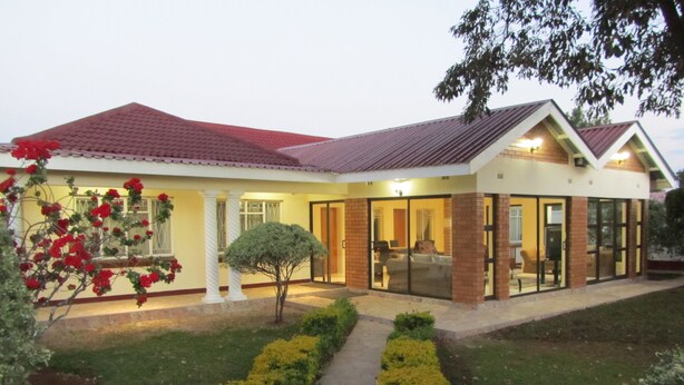 A modern two-story house with a red-tiled roof, large glass doors, and a well-maintained garden with trimmed bushes and a pathway.