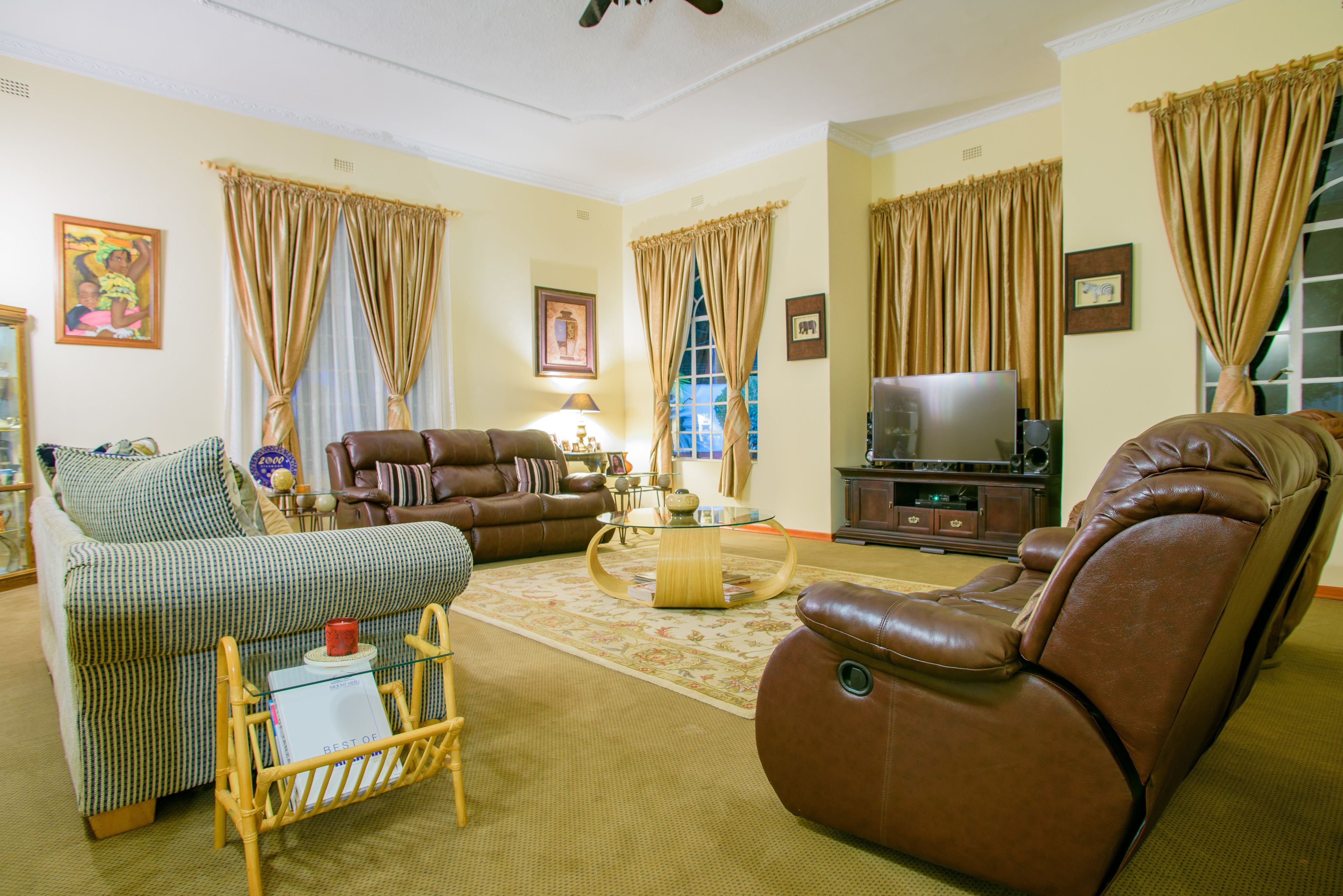 A living room with a brown leather sofa, a green and white striped sofa, a glass coffee table, and a television on a wooden cabinet.
