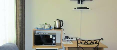 Una kitchenette compacta con microondas, refrigerador y una pequeña mesa con tetera y tazas. Un televisor está montado en la pared sobre la mesa.