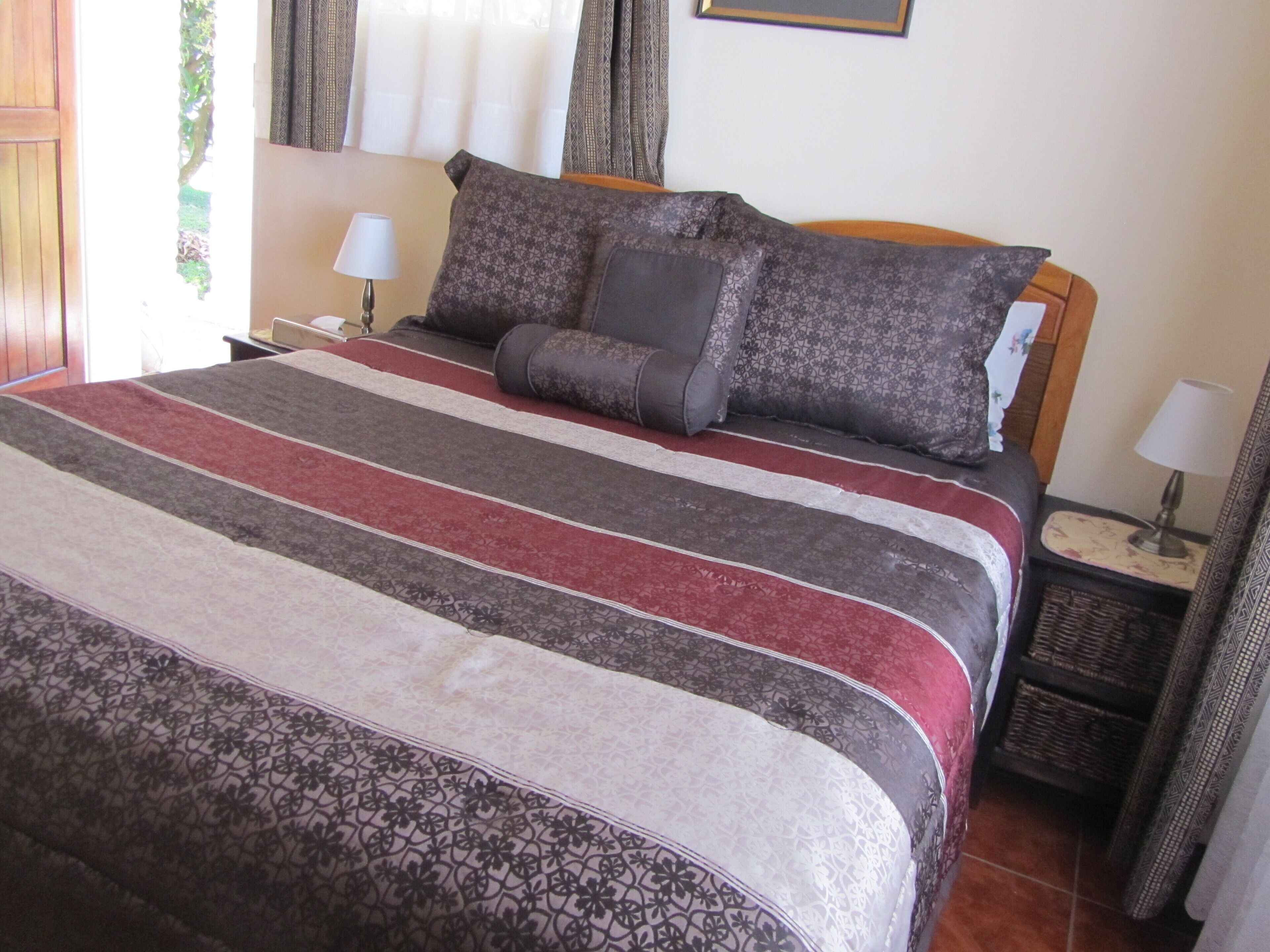Una cama bien tendida con una colcha a rayas, dos mesitas de noche con lámparas y una ventana con cortinas.