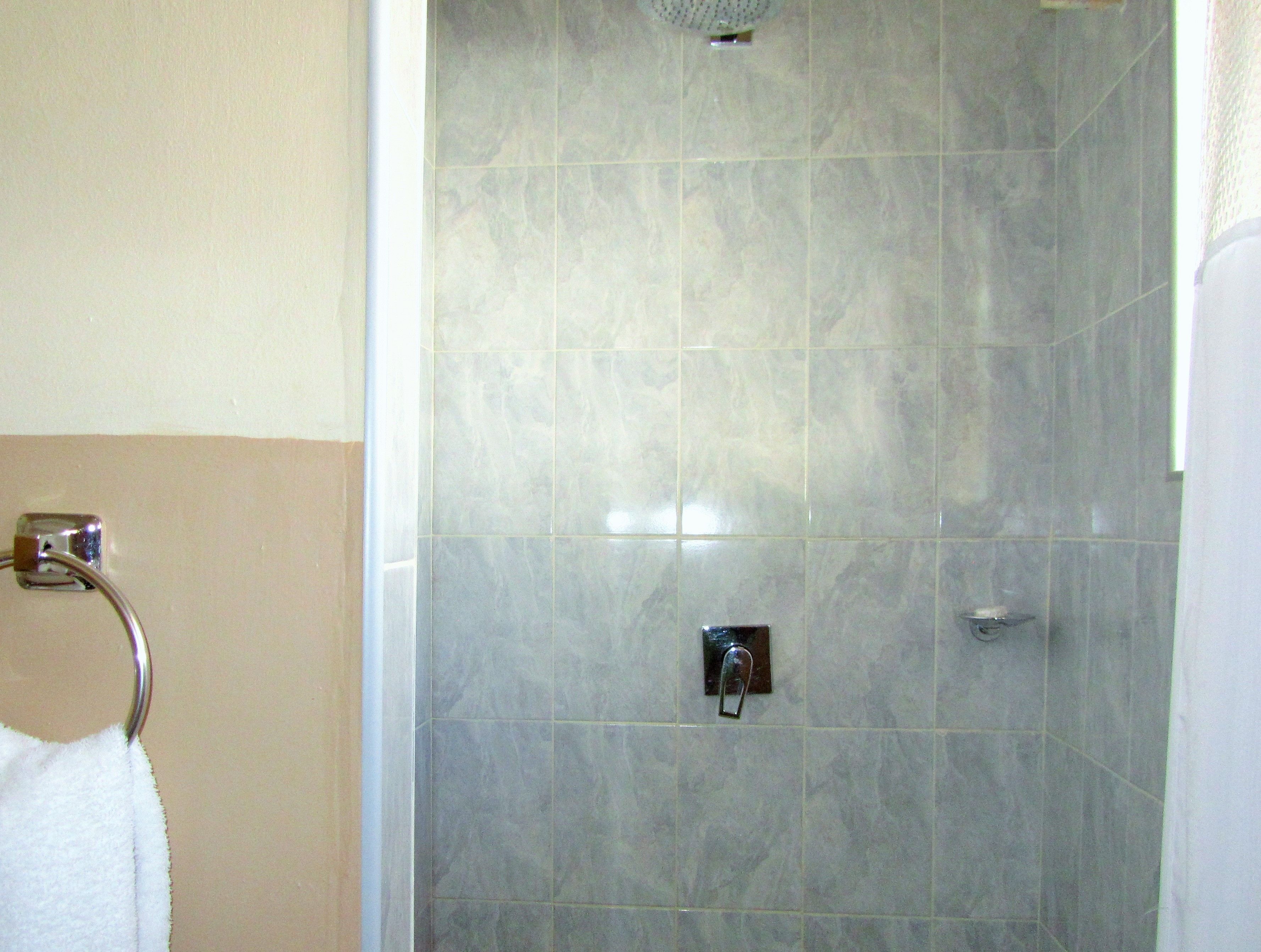 A bathroom with a shower area, a towel rack, and a wall-mounted control panel.