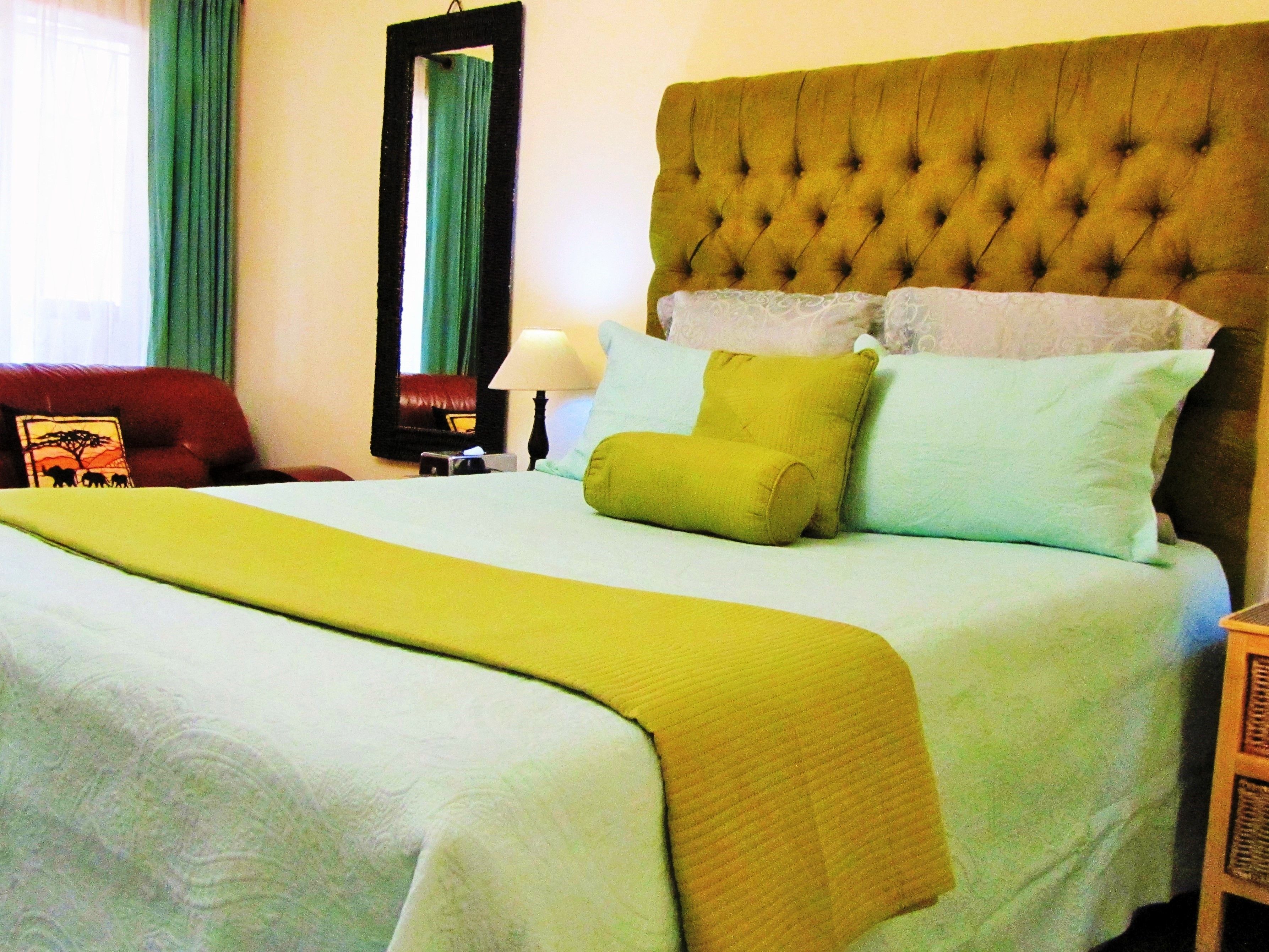 A bed with a tufted headboard, multiple pillows, and a green throw blanket.