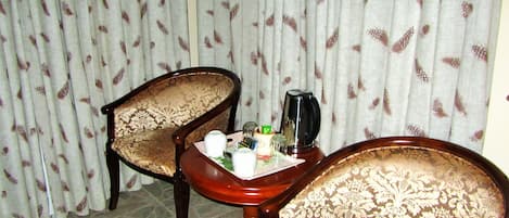 Een kamer met twee houten stoelen en een tafeltje met een theepot, kopjes en een glas.