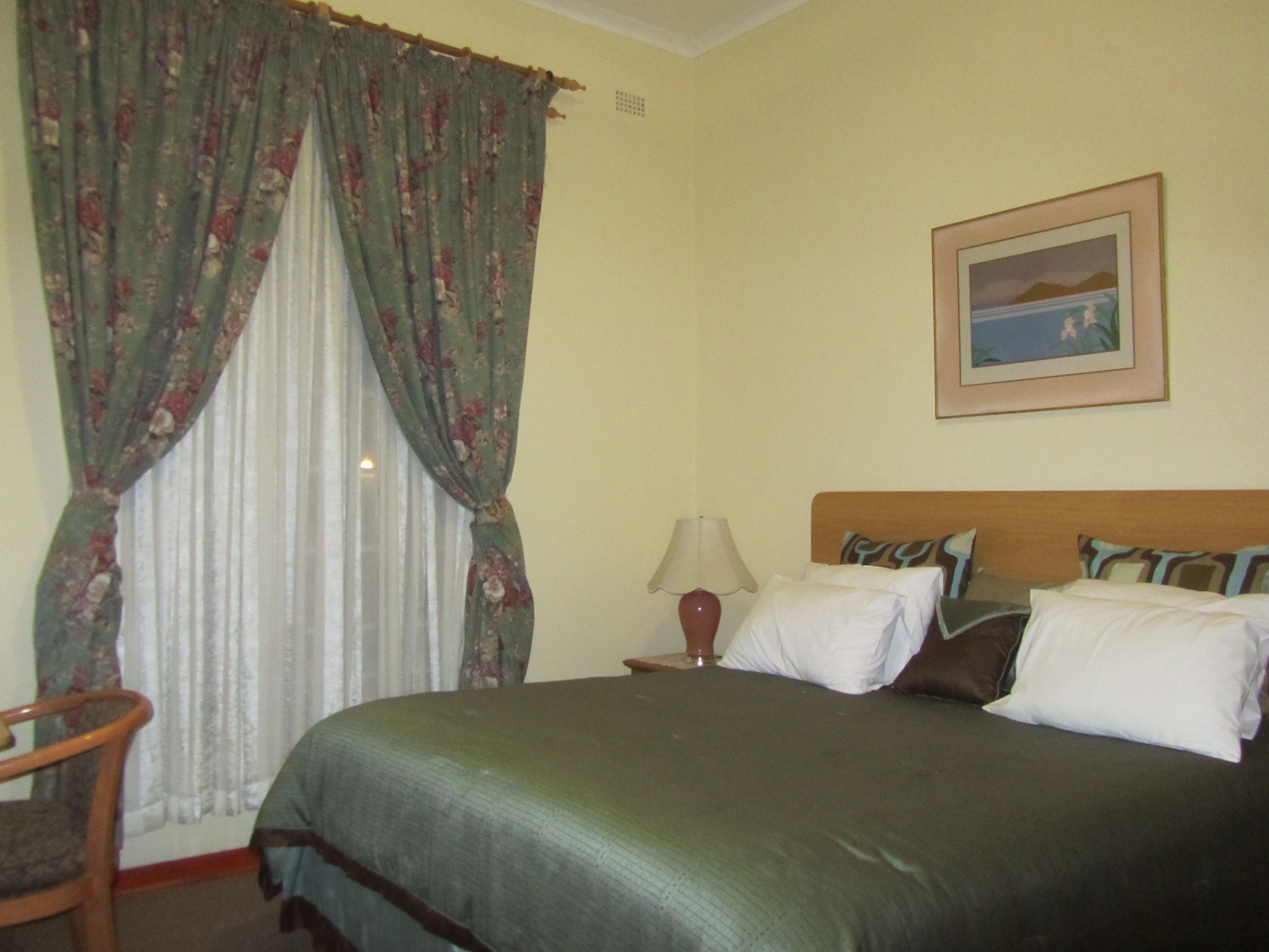 A hotel room with a bed, a chair, a lamp, and a framed picture on the wall.