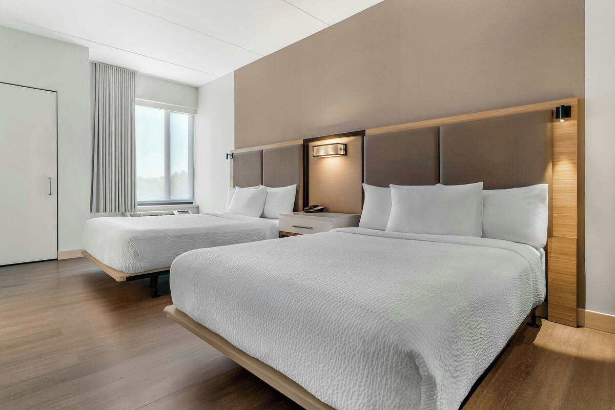 Een hotelkamer met twee bedden, een nachtkastje en een raam met jaloezieën.