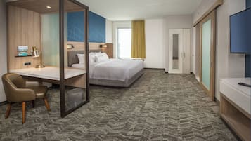 A hotel room with a bed, desk, chair, wardrobe, and a TV.