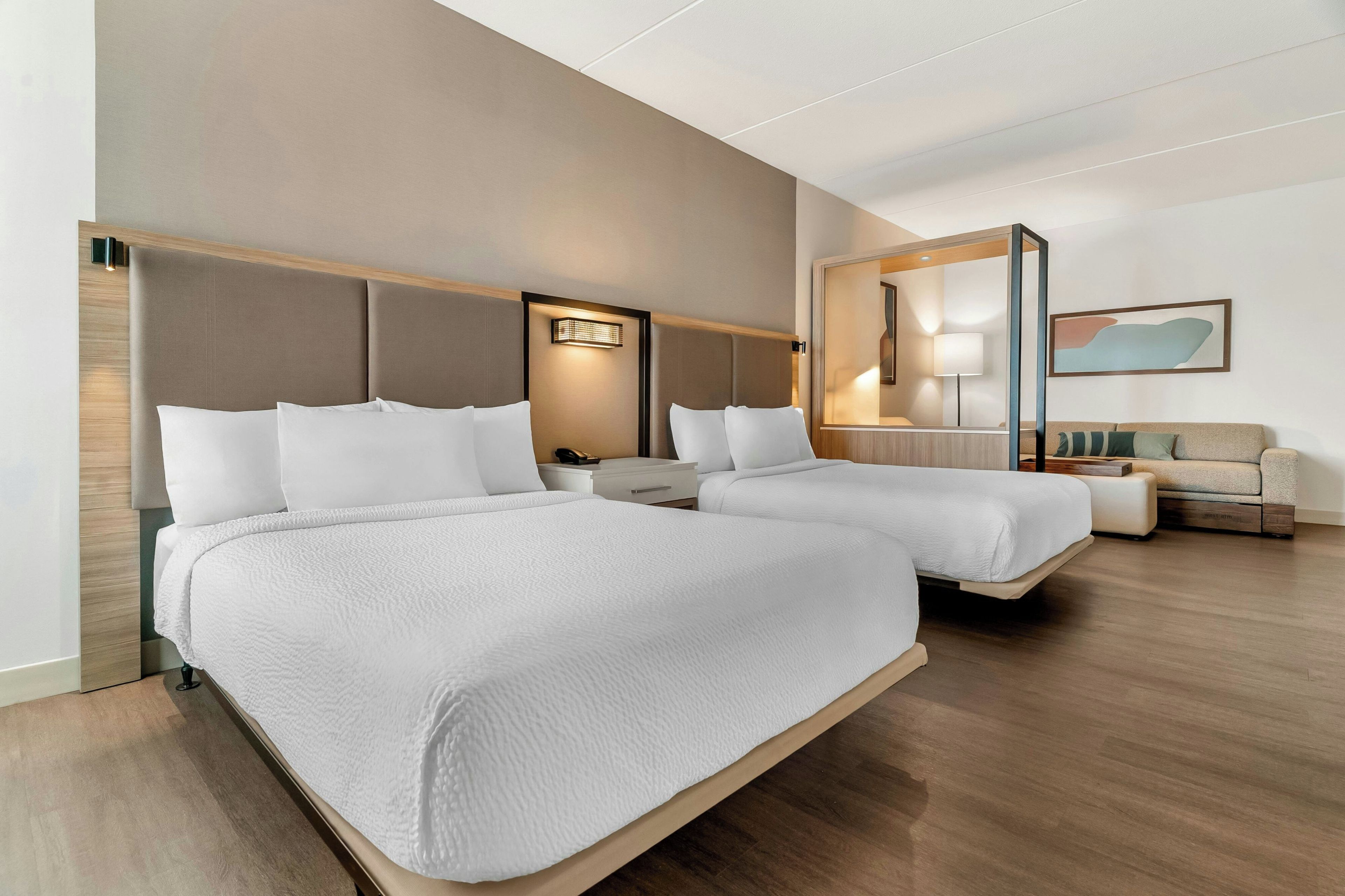 A hotel room with two beds, a sofa, a desk, and a mirror.