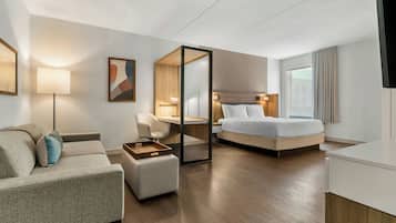 A hotel room with a bed, a desk, a chair, a sofa, and a bedside table.