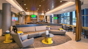A modern lobby with a sectional sofa, round tables, and a bar area. - SpringHill Suites by Marriott Gainesville Haymarket (Gainesville)