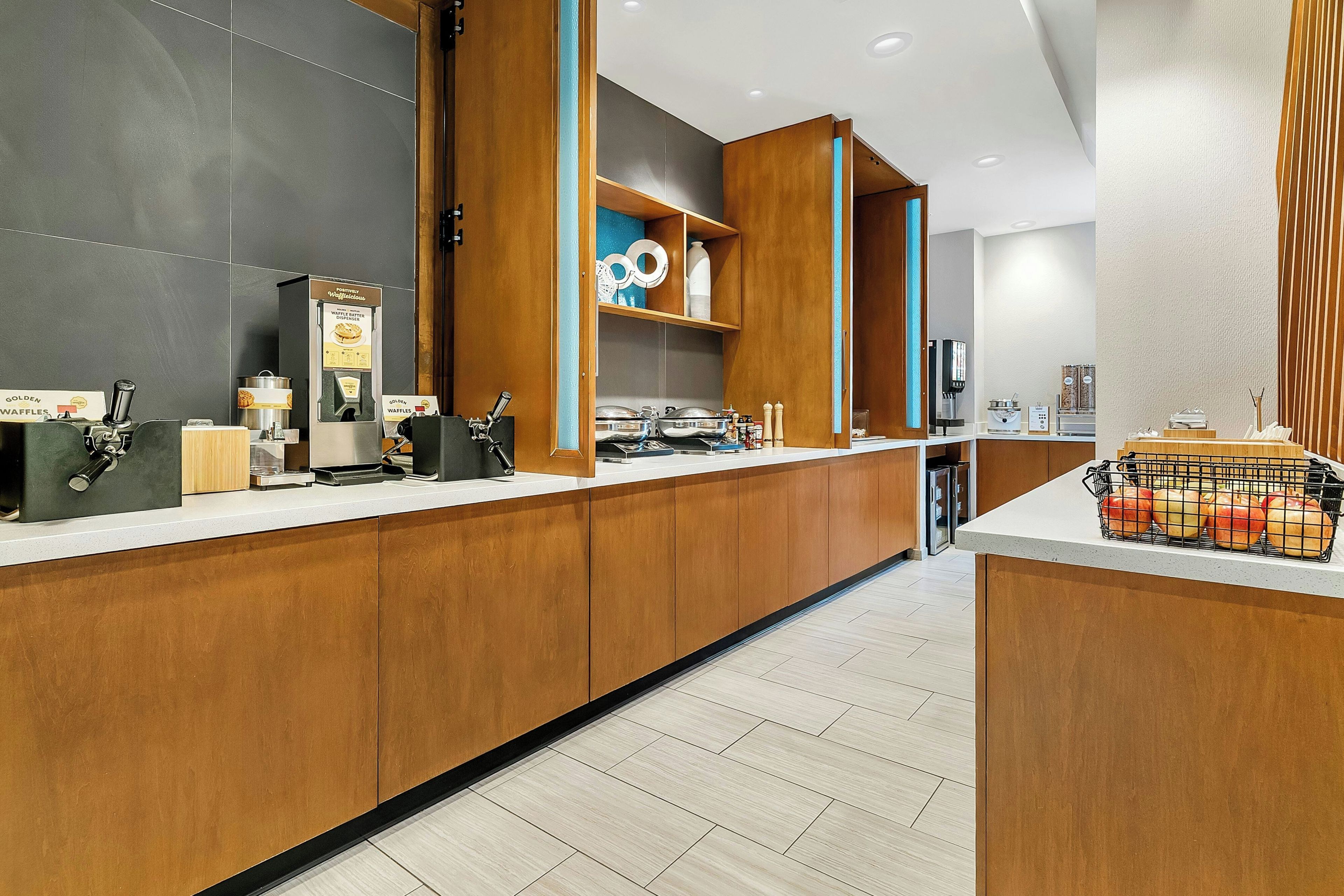 A modern hotel reception area with a wooden counter, a waffle dispenser, and a coffee machine.