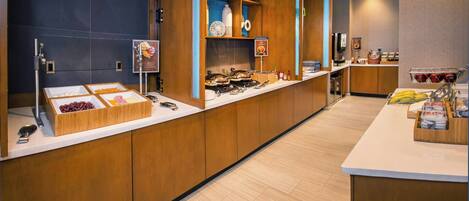 Un área de desayuno de hotel moderna con armarios de madera, una encimera blanca y diferentes opciones de comida.
