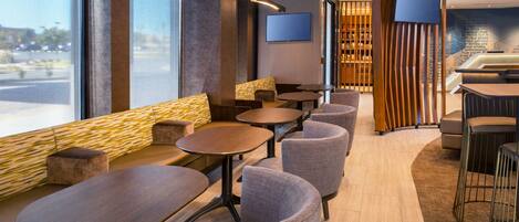 Un restaurante moderno con mesas redondas, asientos acolchados, ventanas amplias y un televisor de pantalla plana en la pared.