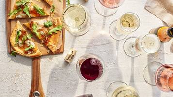 Une planche à pizza en bois, avec des parts de pizza, des verres à vin et un tire-bouchon.