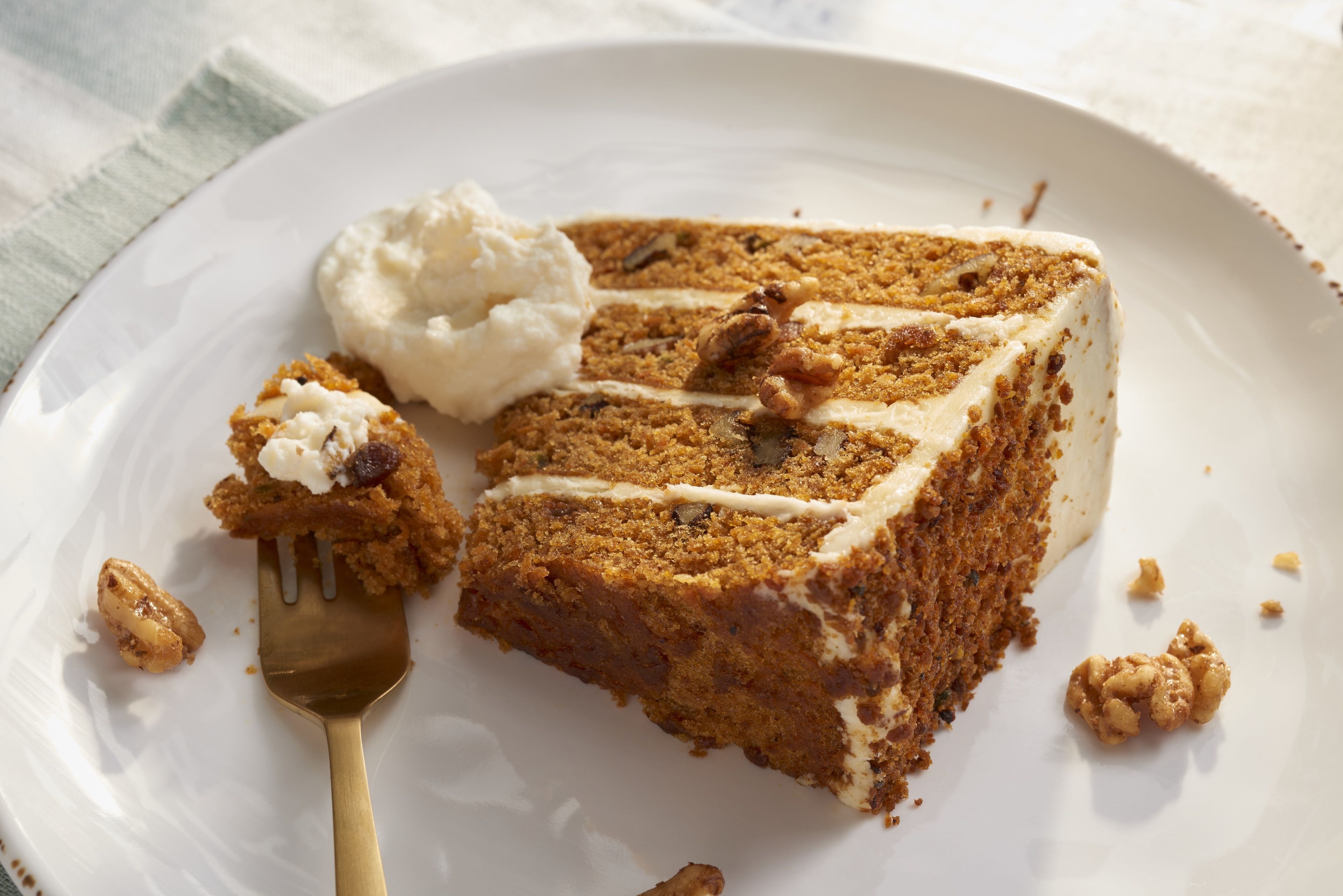 Une part de gâteau aux carottes, recouverte d’un glaçage crémeux, et une boule de glace à la vanille, le tout présenté sur une assiette blanche.