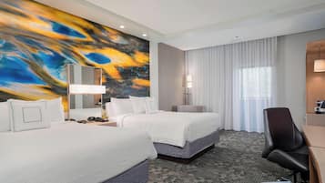 Habitación de hotel con dos camas, un escritorio, una silla, un cuadro abstracto grande en la pared y una ventana con cortinas.