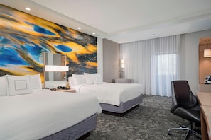 Habitación de hotel con dos camas, un escritorio, una silla, un cuadro abstracto grande en la pared y una ventana con cortinas.