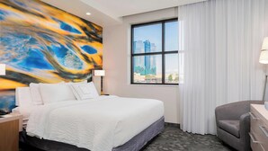 A hotel room with a large bed, a desk, a chair, a window with a city view, and a painting on the wall. - Courtyard by Marriott Niagara Falls USA (Niagara Falls)