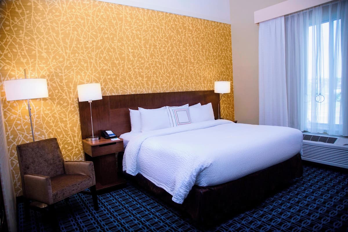 Habitación de hotel con una cama grande, dos lámparas de noche, una silla y un papel tapiz estampado.