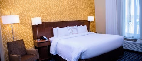 A hotel room with a large bed, two bedside lamps, a chair, and a patterned wall.