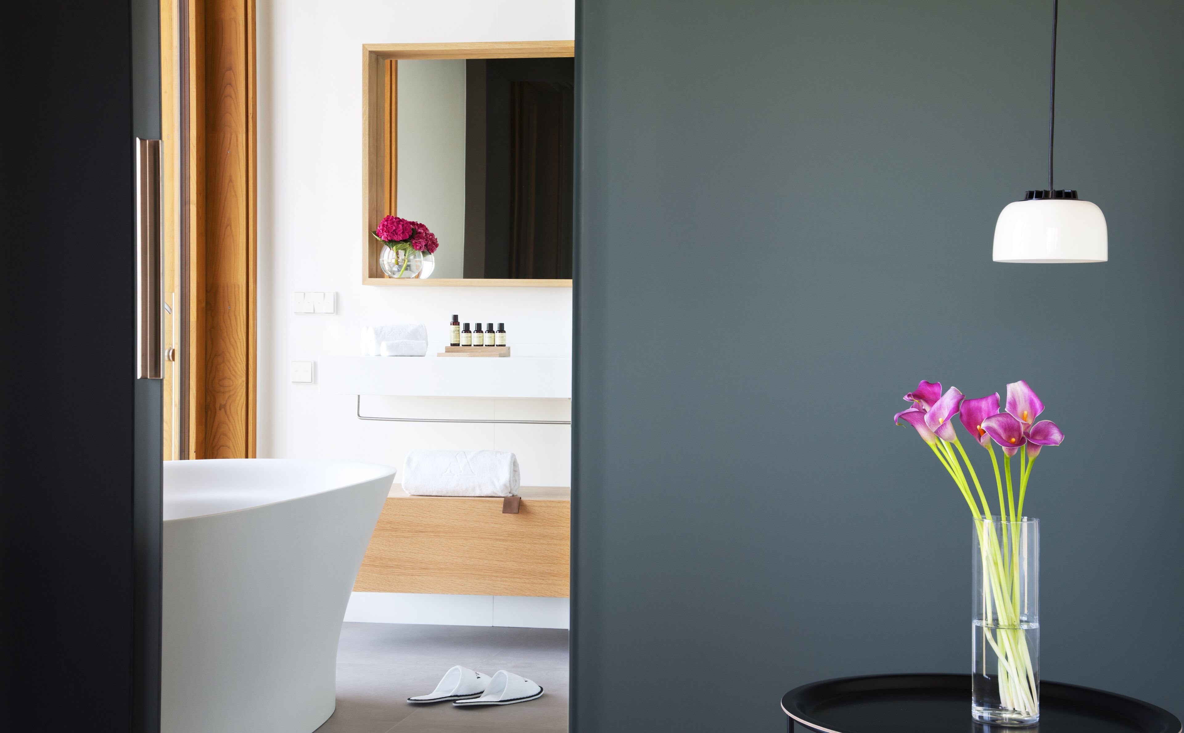 A modern bathroom with a freestanding bathtub, a mirror, and a vanity with toiletries.