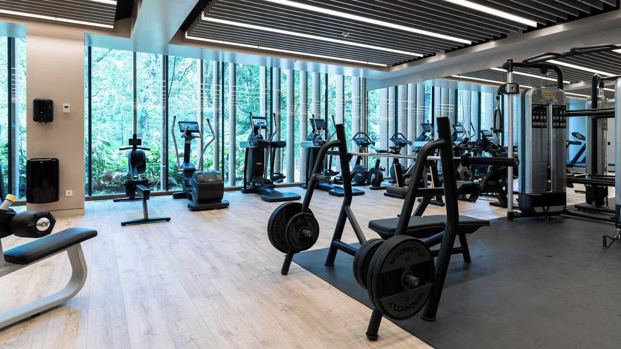 Een moderne sportschool met diverse fitnessapparaten, grote ramen en een houten vloer.
