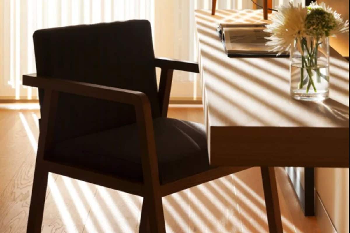 A room with a wooden chair, a small table with a lamp, and a vase with flowers.
