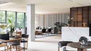 En moderne hotellobby med et siddeområde, en receptionsdisk og et stort vindue med udsigt over grønne områder.