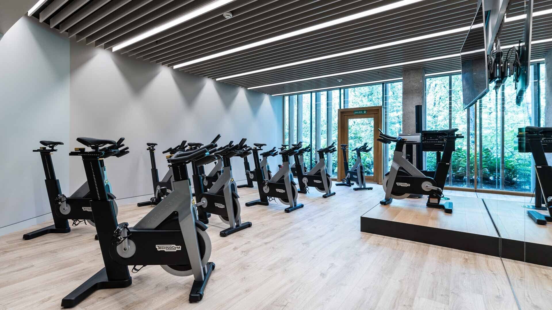 Une salle de sport dotée de nombreux vélos d’appartement disposés en rangées, de grandes fenêtres et d’un design moderne au niveau du plafond.