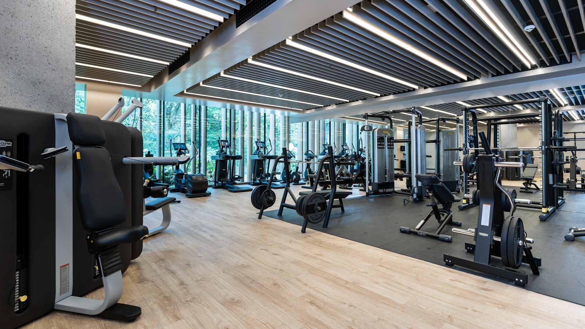 Ein modernes Fitnessstudio mit unterschiedlichen Trainingsgeräten, großen Fenstern und Holzboden.