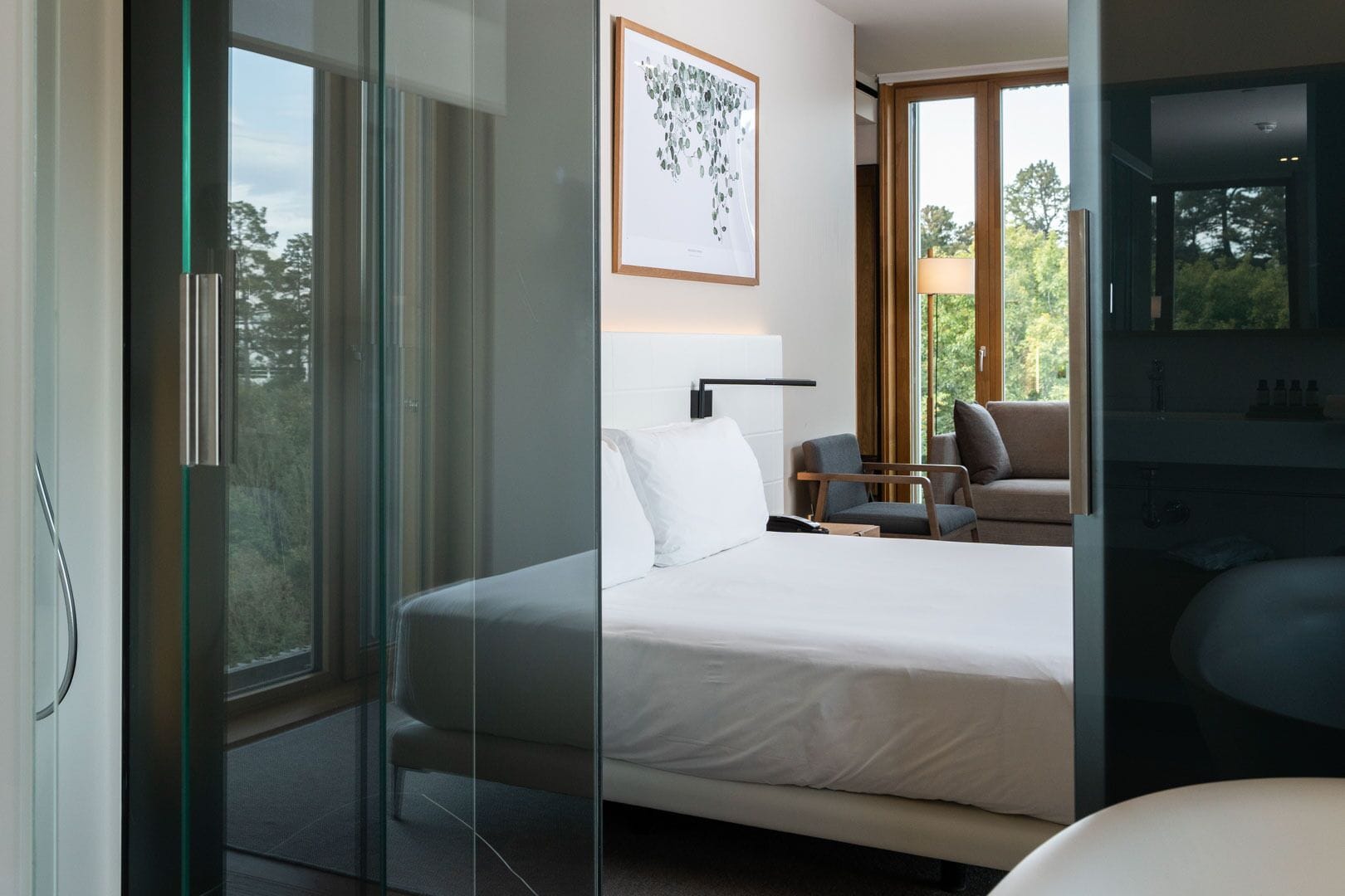 A modern bedroom with a large bed, a desk, and a chair. There is a window with a view of trees.