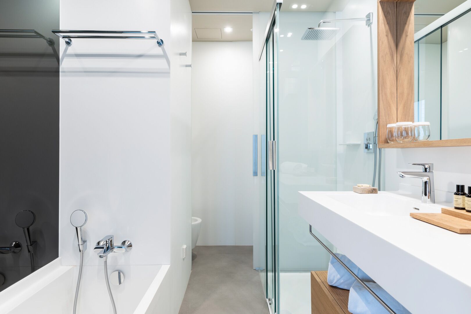 Een moderne badkamer met een douchecabine van glas, een witte wastafel met een houten aanrechtblad en een spiegel boven de wastafel.
