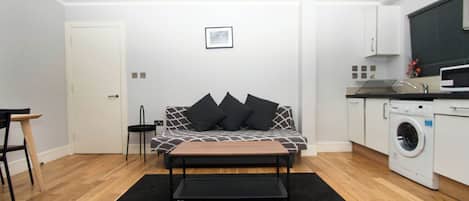 Un espacio habitable moderno y funcional con sofá, mesa de centro, lavadora y pequeña cocina.