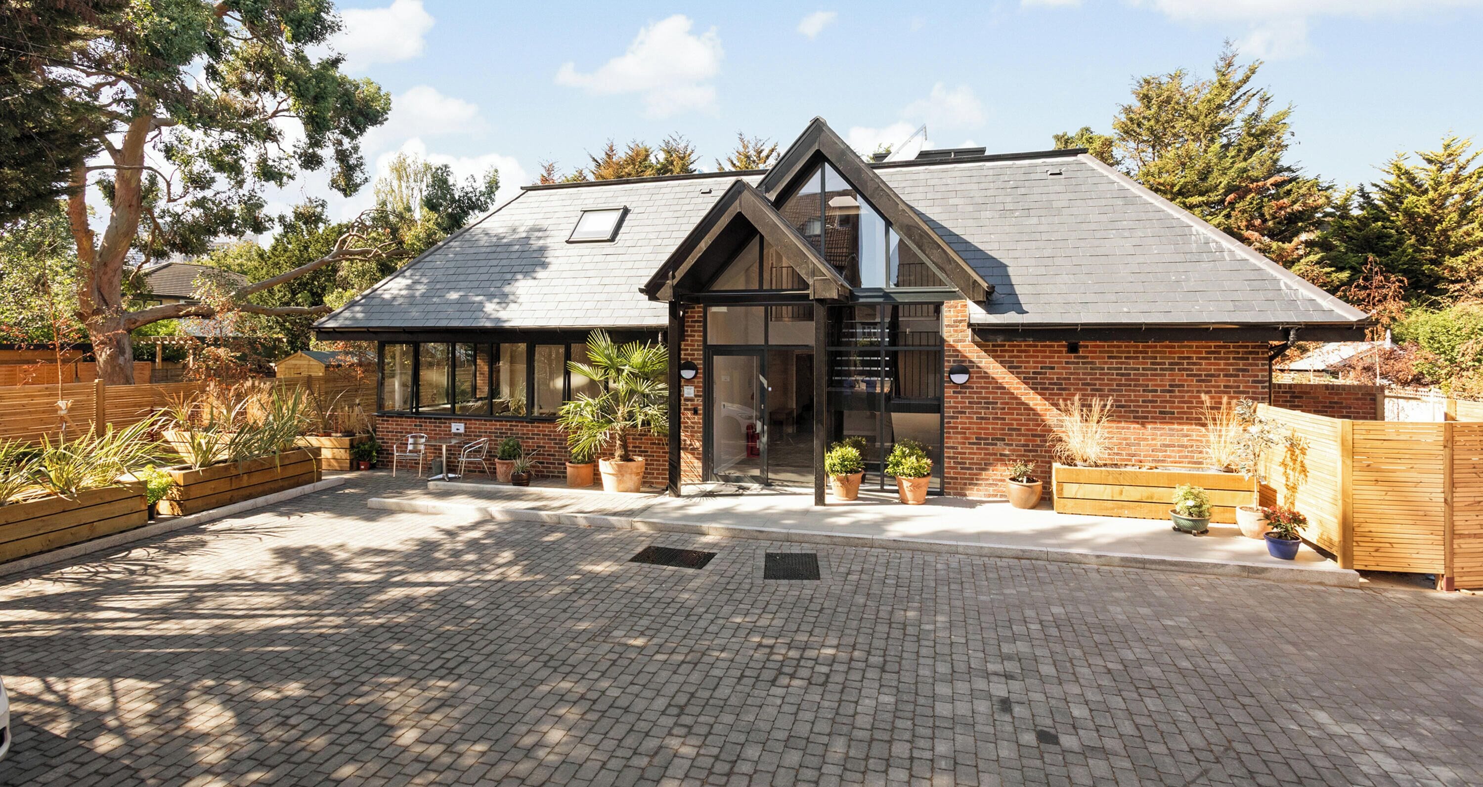 A Caroco Garden Suites building with a brick exterior, large windows, and a paved entrance area with potted plants.