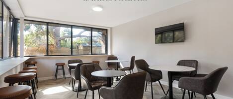 A modern interior with a bar area, multiple seating arrangements, and large windows providing natural light.