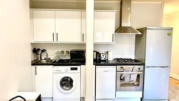 A compact kitchen with white cabinets, a washing machine, a dishwasher, a stove, and a refrigerator.