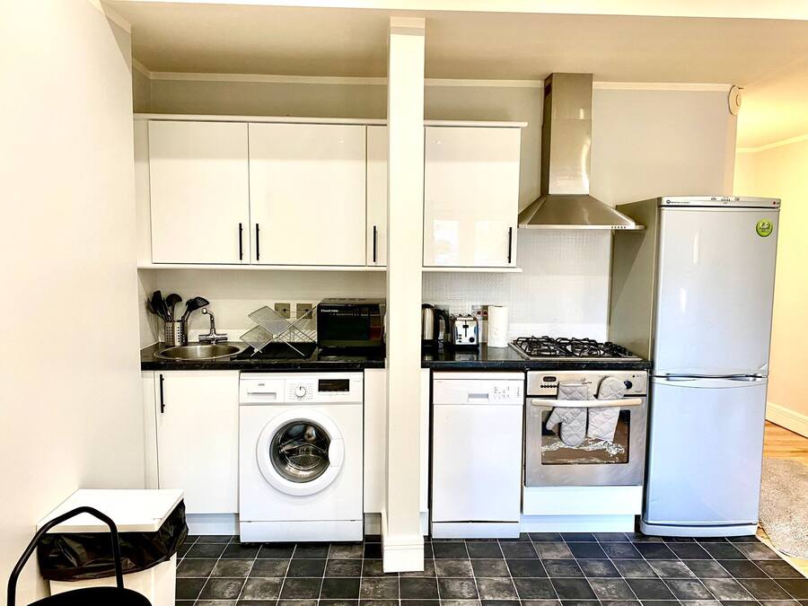 A compact kitchen with white cabinets, a washing machine, a dishwasher, a stove, and a refrigerator.