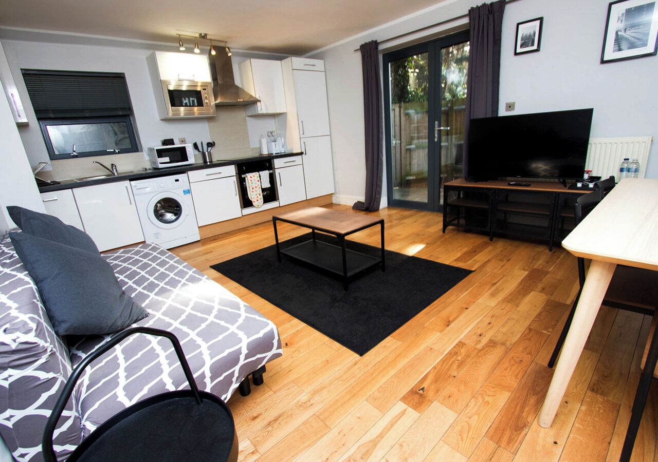 Ein kompakter Wohnbereich mit Sofa, Couchtisch, Fernseher, Waschmaschine und einer Küchenzeile.