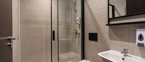 Un baño moderno con ducha envuelta en vidrio, un lavamanos blanco y un inodoro.