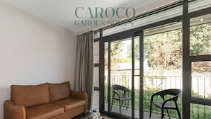 A living room with a brown sofa, a small round table with a tray, and two chairs on a balcony with a view of greenery. - Westciti Caroco Aparthotel (Croydon)