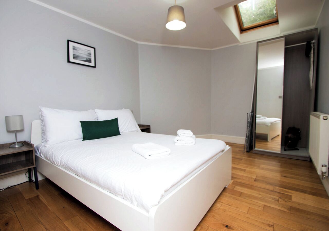 A modern bedroom with a large bed, a bedside table, a lamp, and a framed picture on the wall.