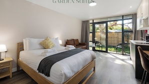 A bedroom with a large bed, a desk, and a view of the garden. - Westciti Caroco Aparthotel (Croydon)