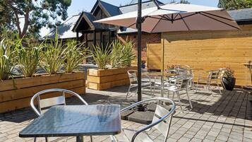 An outdoor patio with metal tables and chairs, wooden planters with plants, and a large umbrella.