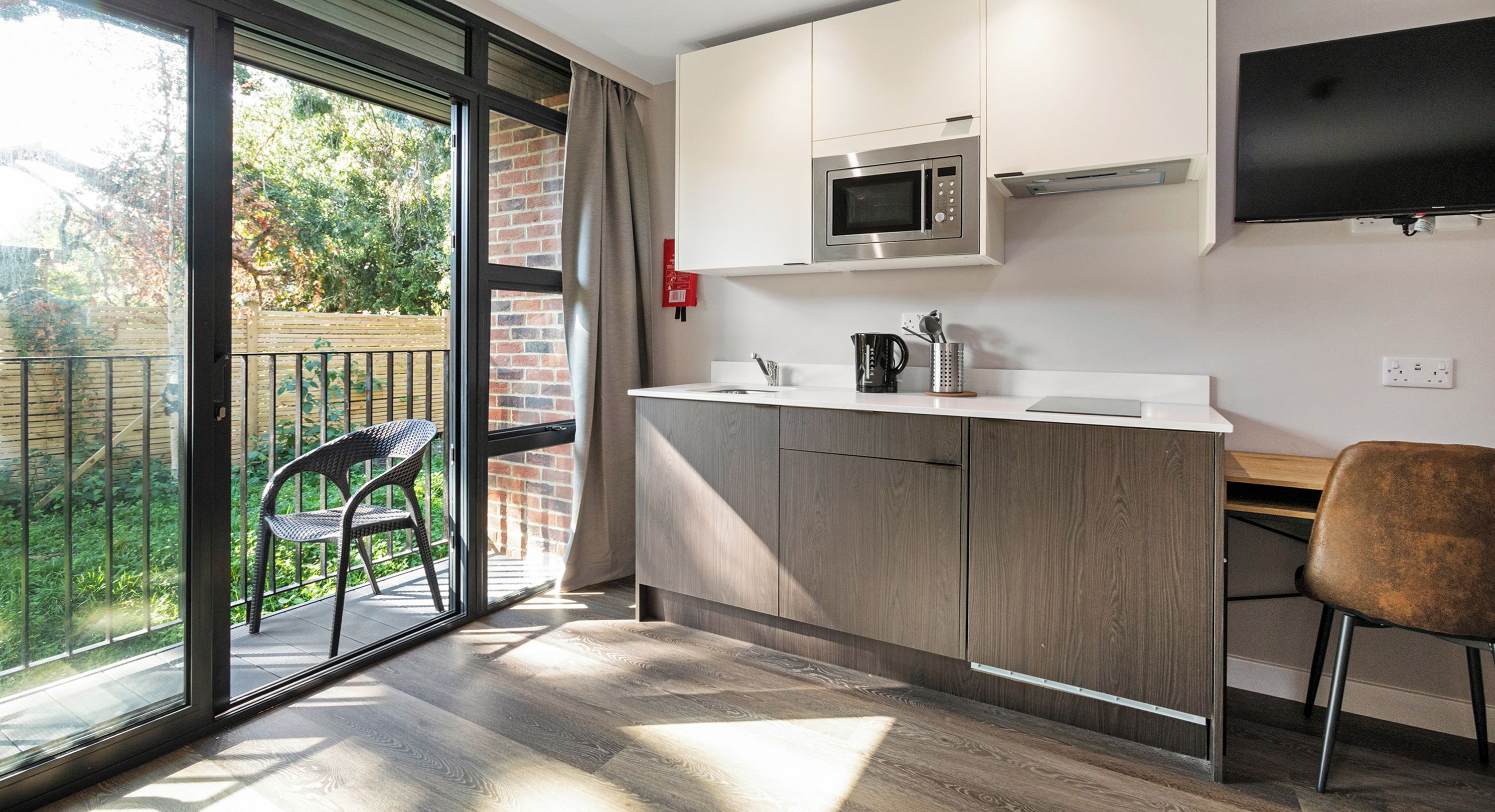 A modern kitchen with a built-in microwave, a flat-screen TV, and a sliding glass door leading to a balcony.