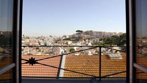 Vista desde una ventana con vista a un paisaje urbano con tejados de tejas y edificios a lo lejos.