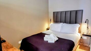 A neatly made bed with a dark headboard, a bedside table with a lamp, and a small table with a knife and a bottle.