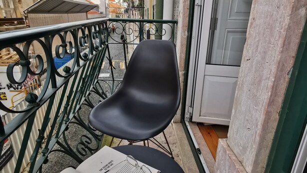 Un balcón con dos sillas negras, una mesa con un libro, una taza y una cuchara.