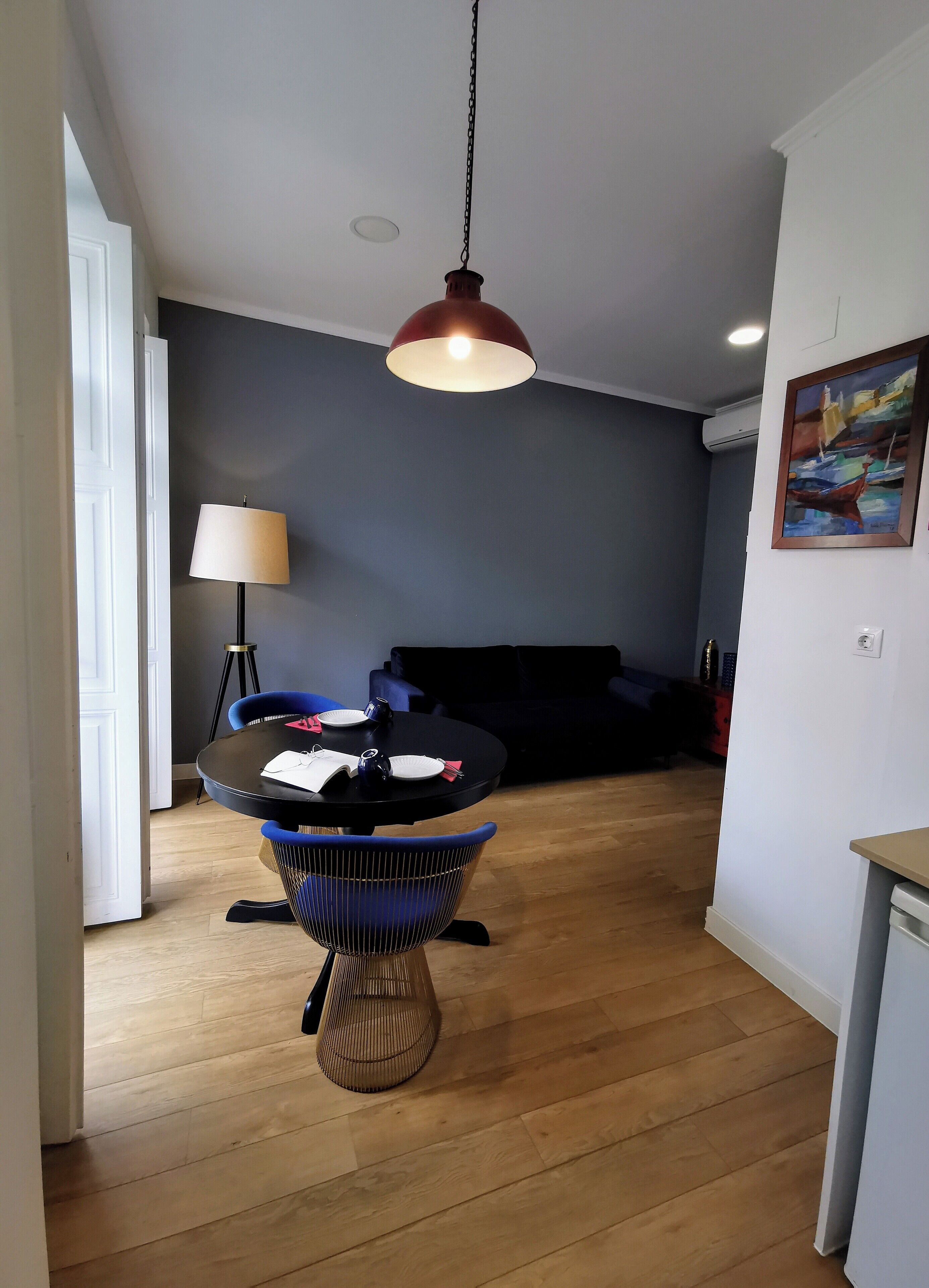 A modern living room with a round dining table, a blue chair, and a red pendant light.